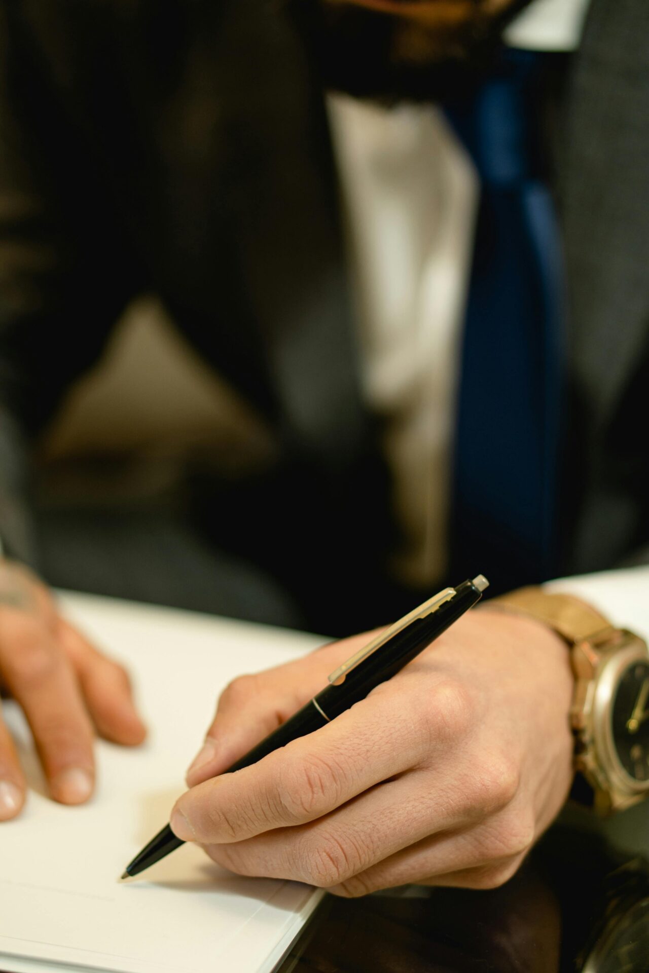 Close-up of a person signing a document with a formal pen, wearing a suit and watch